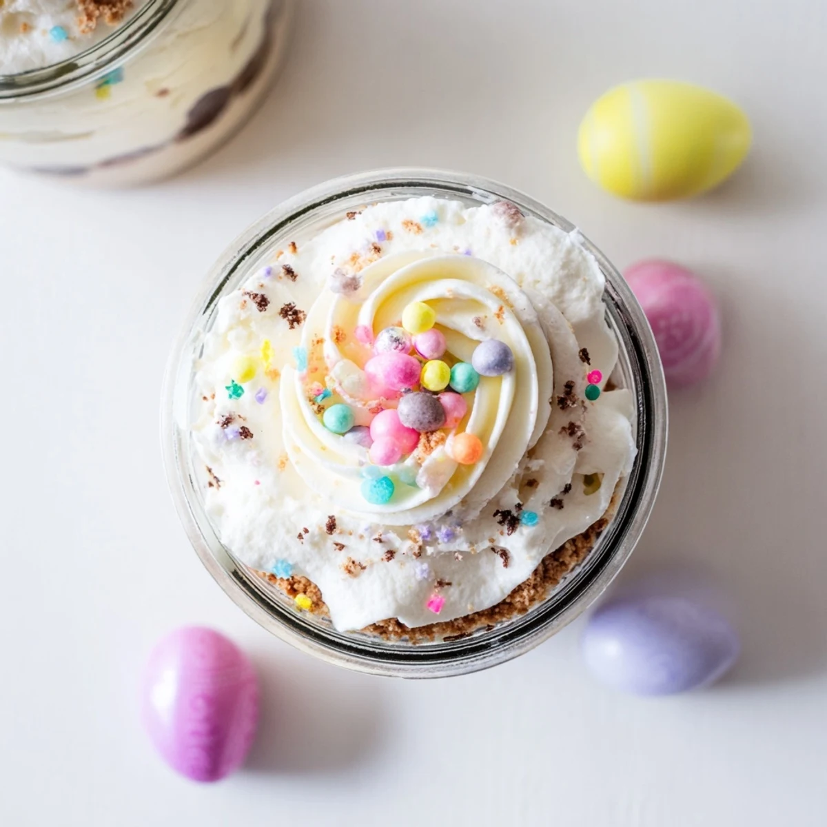 Glass jars layered with creamy Easter Egg Cheesecake topped with whipped cream and pastel sprinkles