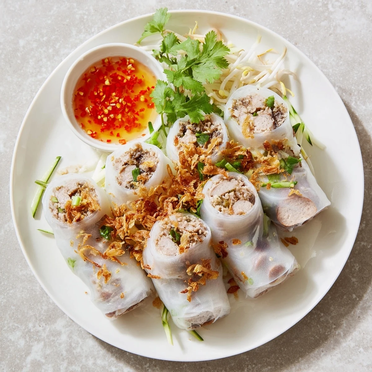 Vietnamese Banh Cuon breakfast dish topped with fried shallots and served alongside tangy dipping sauce