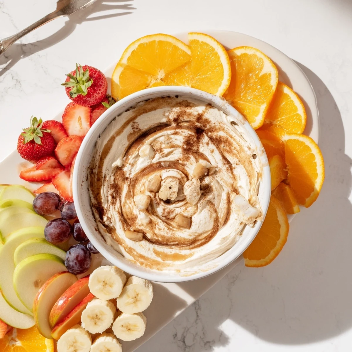 Creamy Greek yogurt cinnamon roll dip swirled with cinnamon and served with fresh apple slices, strawberries, and grapes for a healthy protein-packed snack