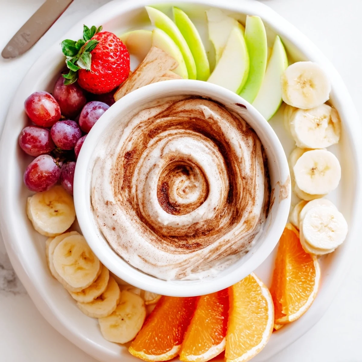 Protein-rich Greek yogurt cinnamon roll dip with marbled cinnamon swirl topping alongside colorful fresh fruit dippers arranged on a serving platter