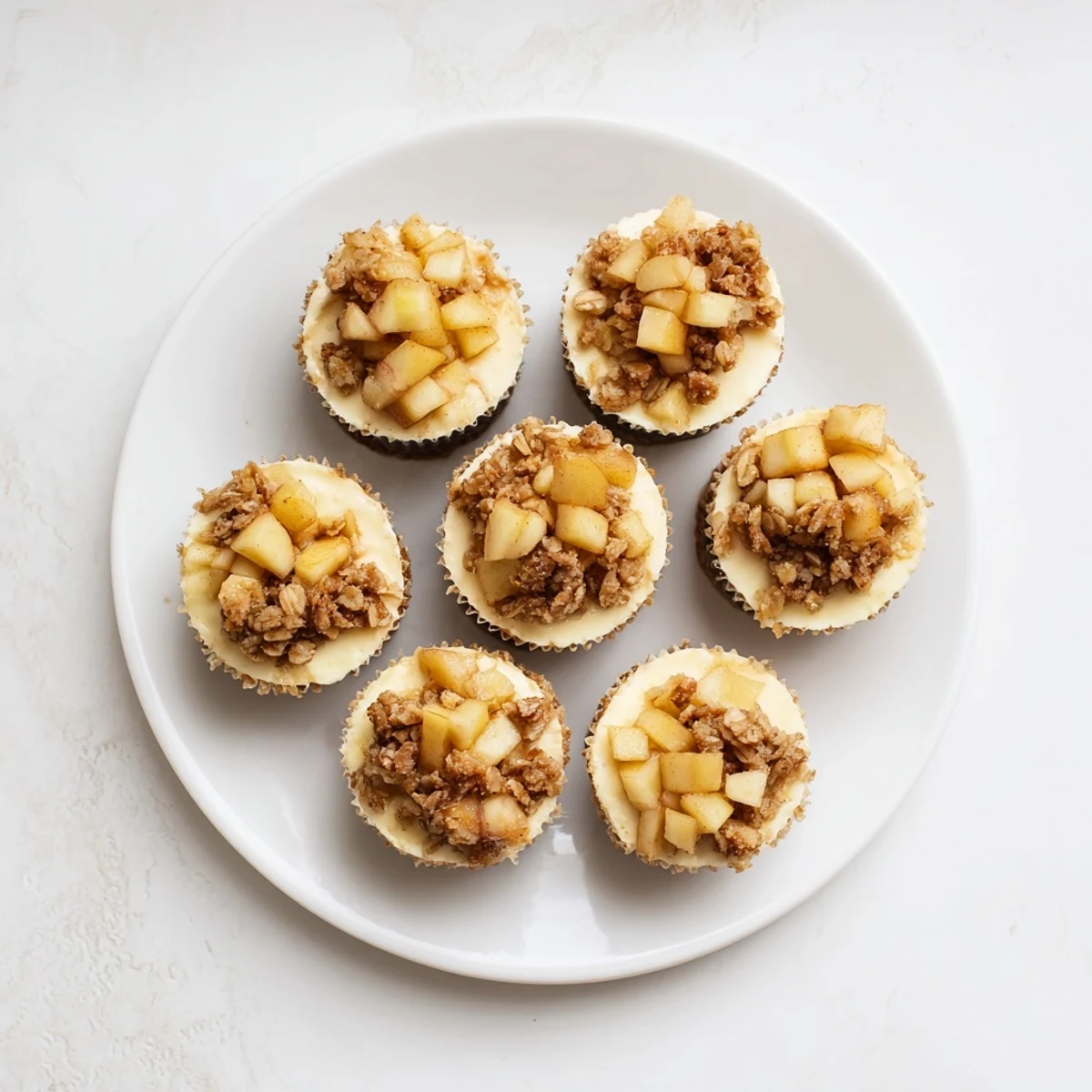 Individual creamy cheesecakes with graham cracker crusts piled high with tender caramelized apple topping