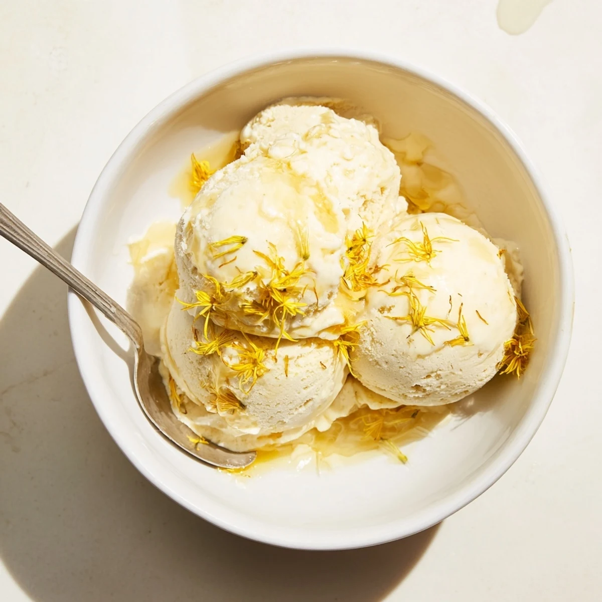 Golden dandelion honey ice cream swirling in a glass bowl with fresh edible garnish