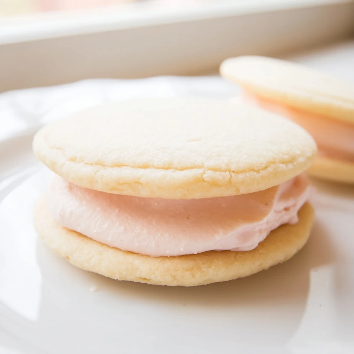 Pastel Sugar Cookie Sandwiches with swirled buttercream filling on a rustic white serving board