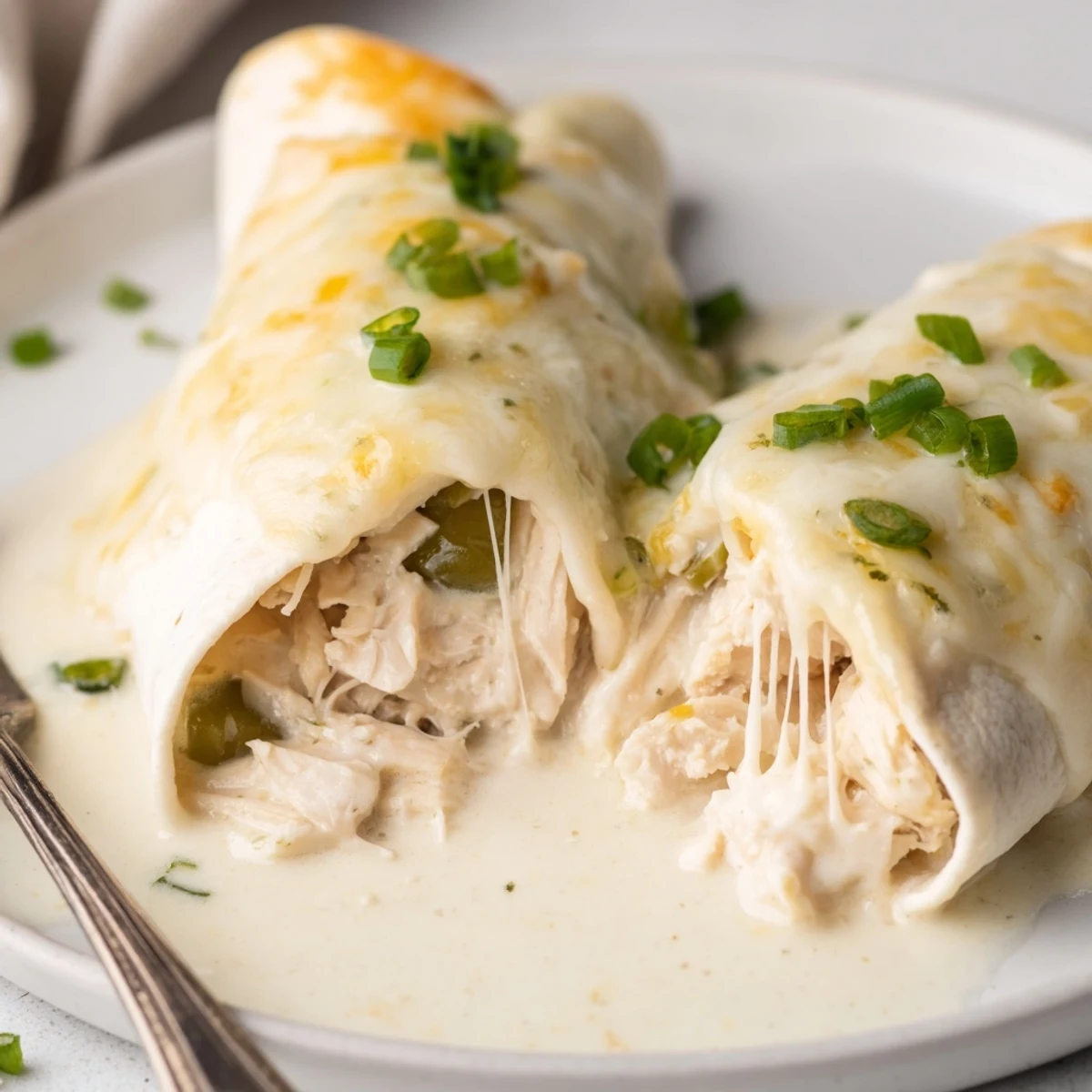 Creamy White Chicken Enchiladas bubbling in a golden sauce, garnished with cilantro.