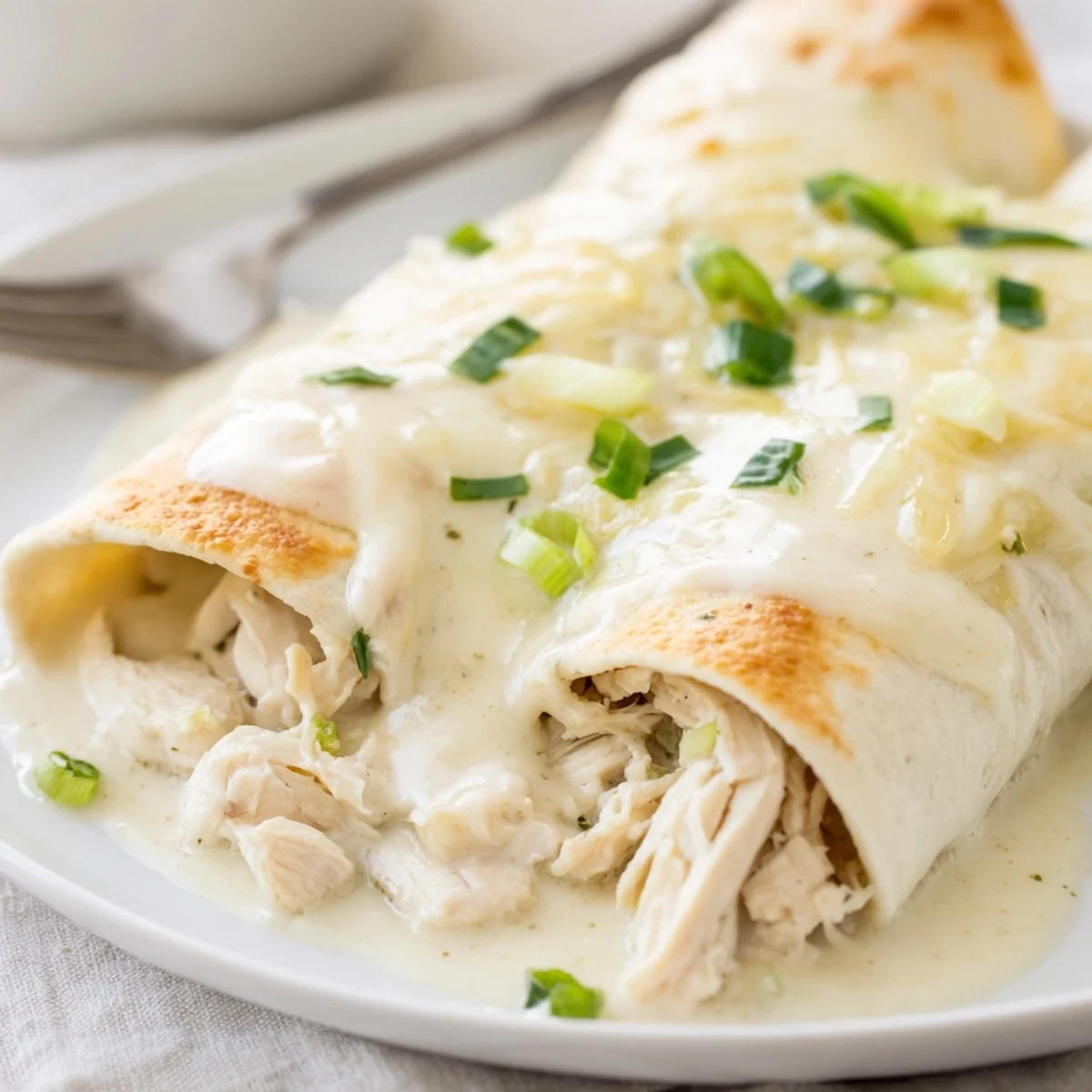 Plate of Creamy White Chicken Enchiladas served with lime wedges and rice.